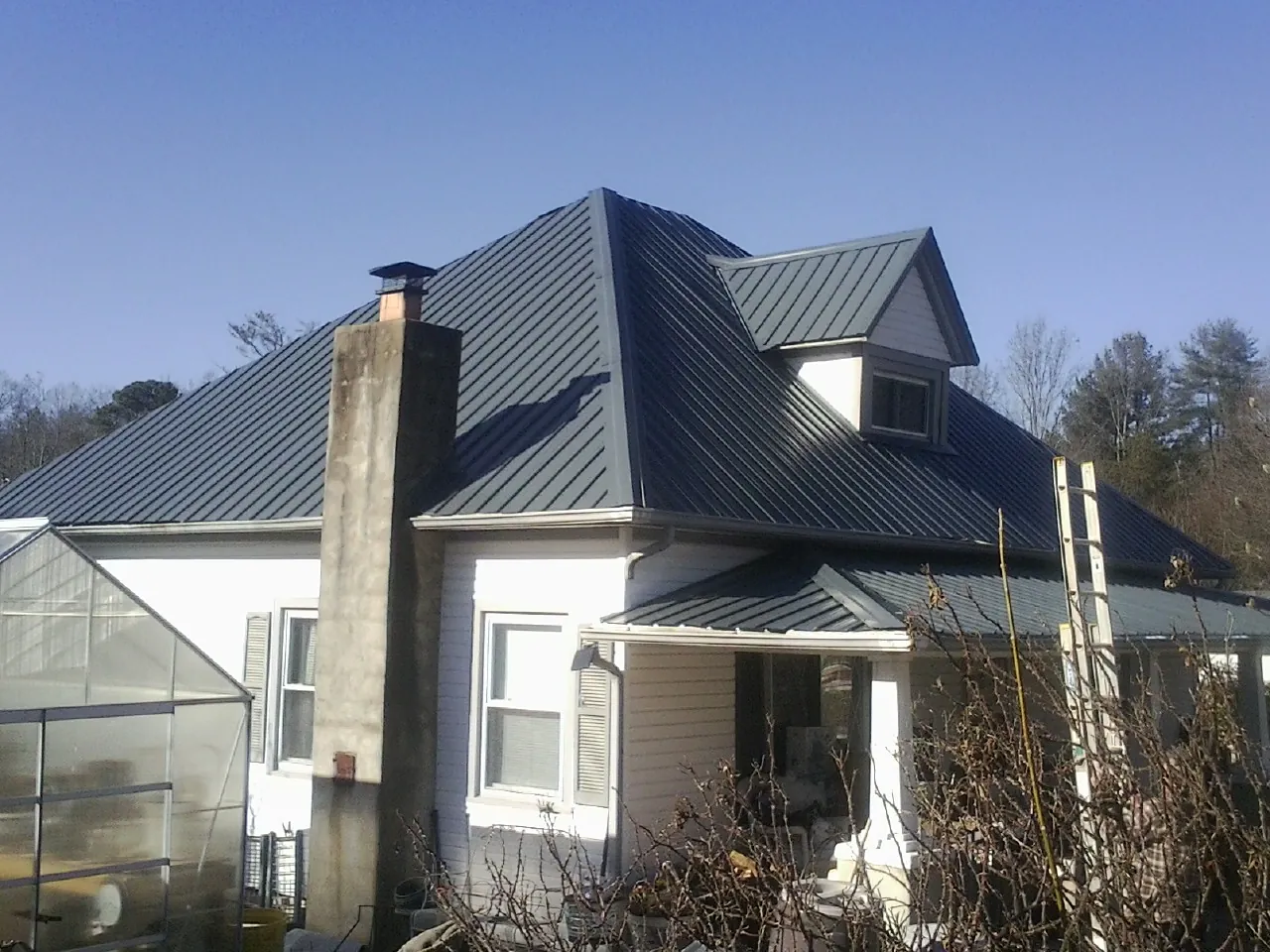Dark blue standing seam metal roof on a white farmhouse with dormer — Slate & Tile Roof Repair by Roofing Brothers in Galt