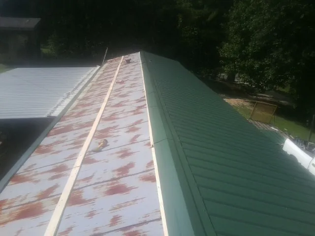 Old rusted panels beside newly installed green metal roofing — Wind Damage Roof Repair by Roofing Brothers in Galt