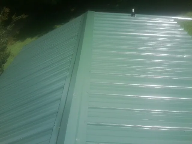 New green metal panels meeting at the ridge of a roof — Flat Roof Repair work by our crew in Galt
